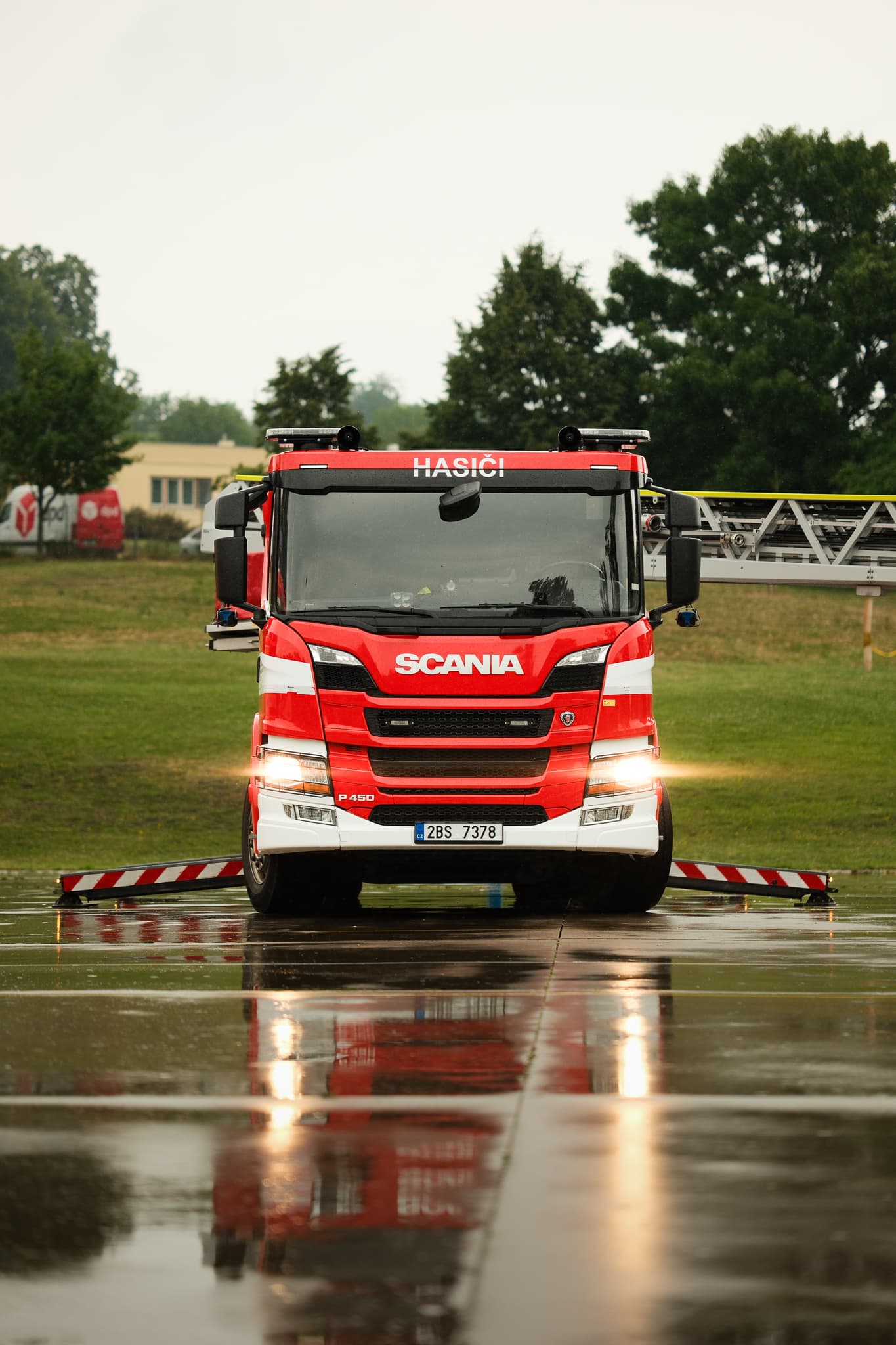 Červené hasičské vozidlo Scania s výsuvným žebříkem na mokré ploše za deště