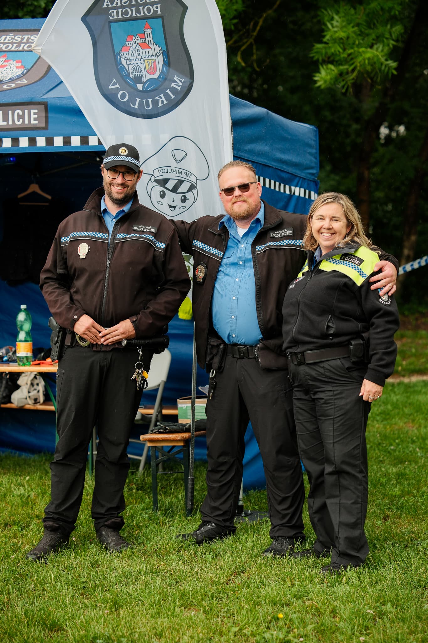 Tři usměvaví strážníci městské policie pózují před svým stánkem