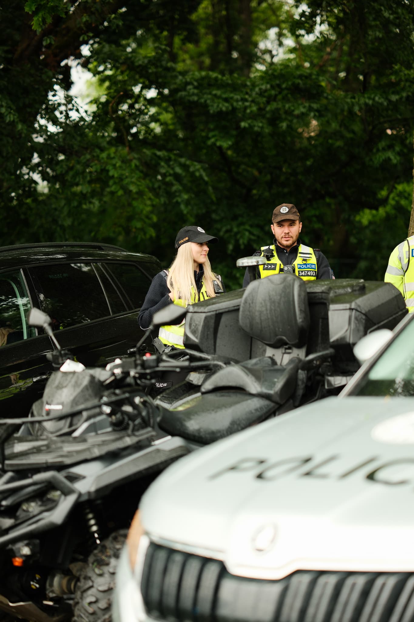Policisté v reflexních vestách u zásahové čtyřkolky a vozů v parku
