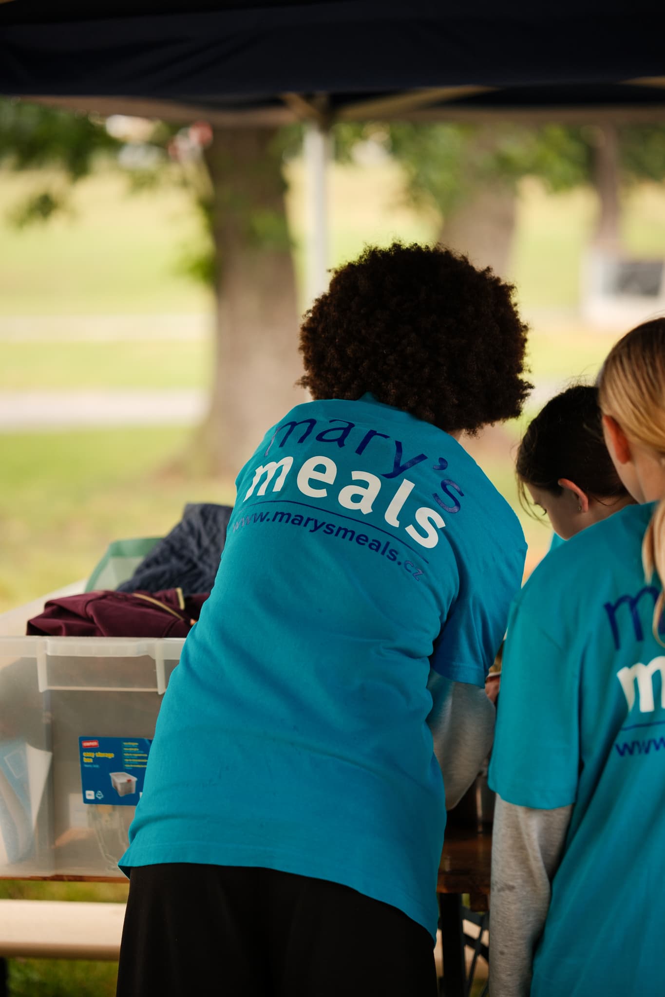 Dobrovolnice charity Mary's Meals připravují stánek pod přístřeškem