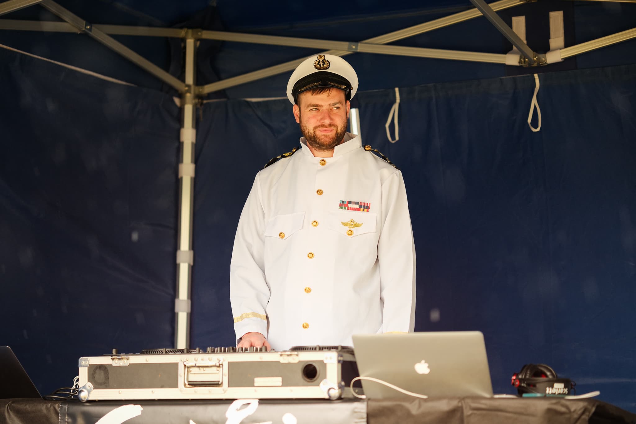 DJ v bílé kapitánské uniformě za mixážním pultem pod stanem