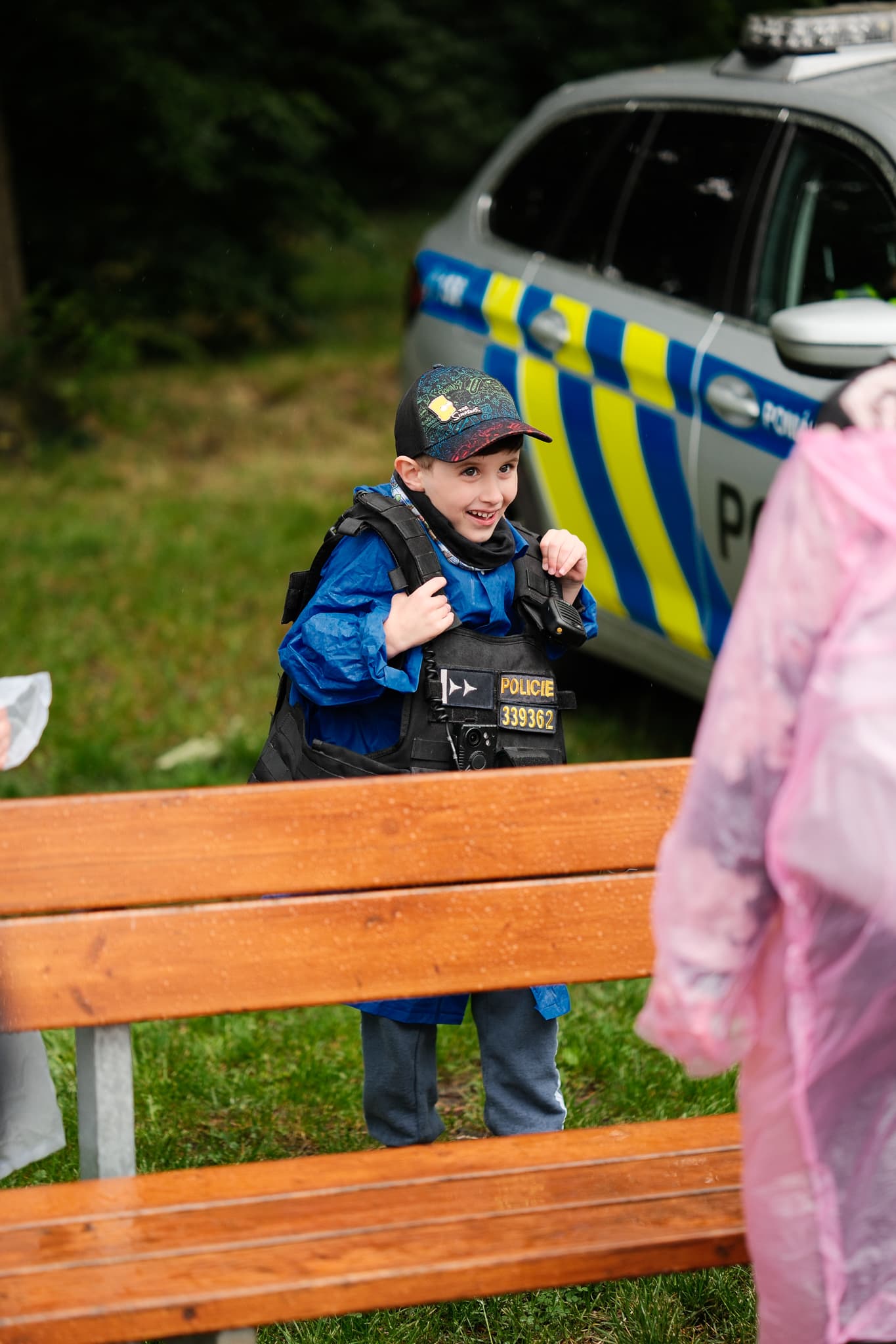 Nadšený chlapec ve velké policejní neprůstřelné vestě u služebního vozu
