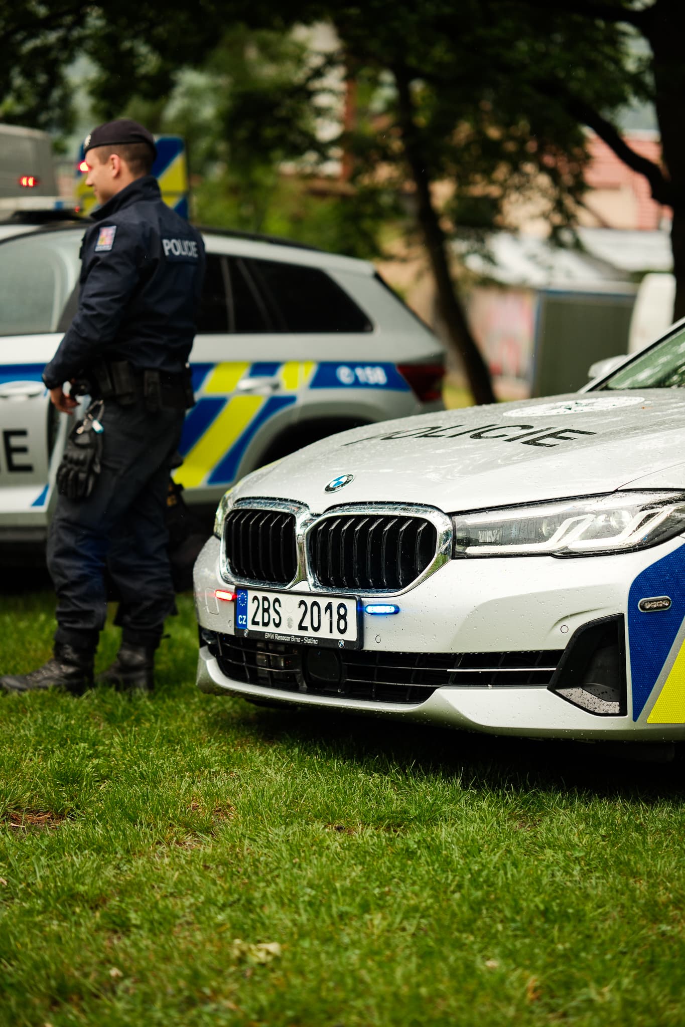 Policista hlídá řadu služebních vozů včetně bílého BMW na trávníku