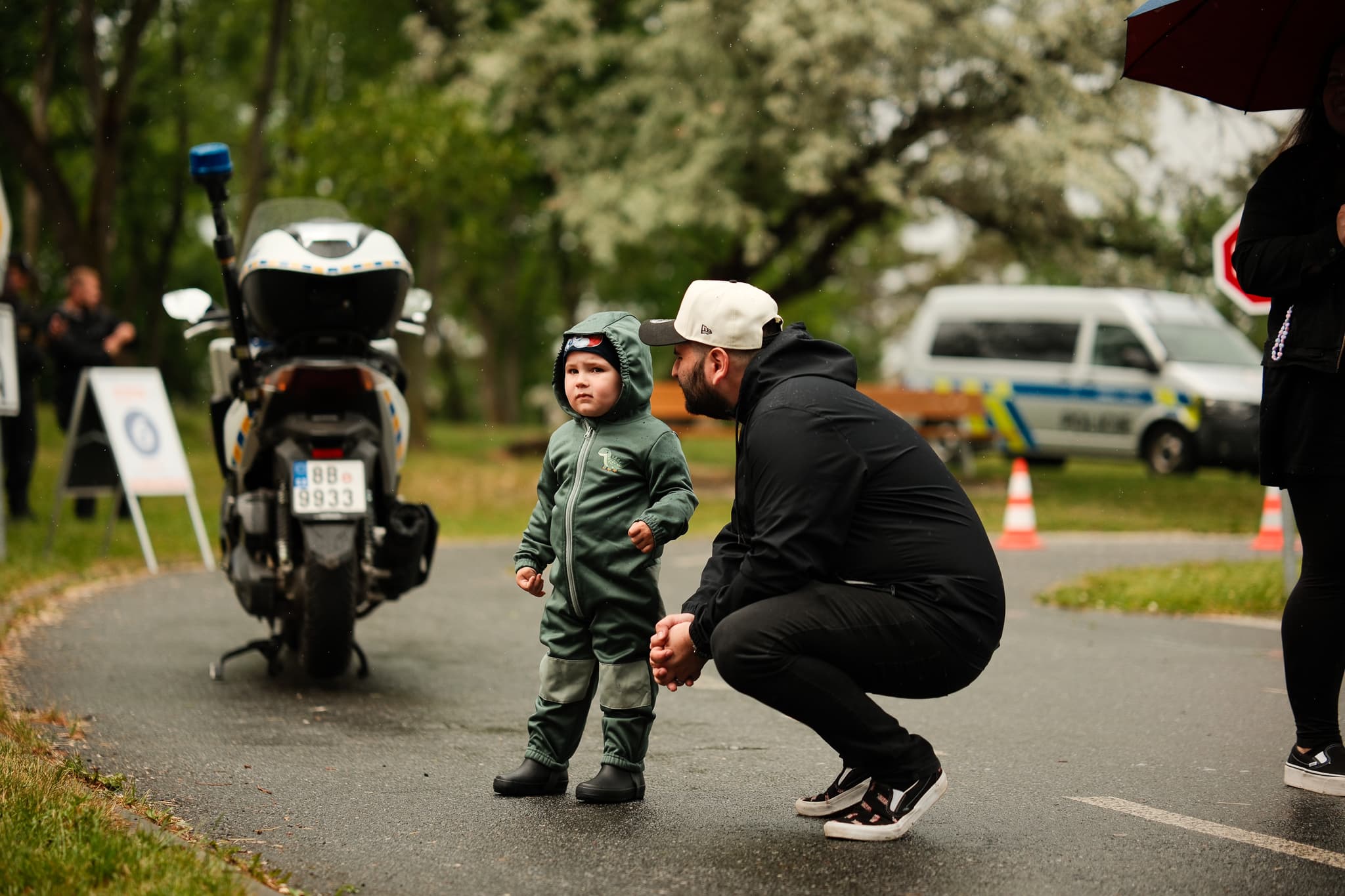 Tatínek se v dešti sklání k batoleti u policejního motocyklu na trati