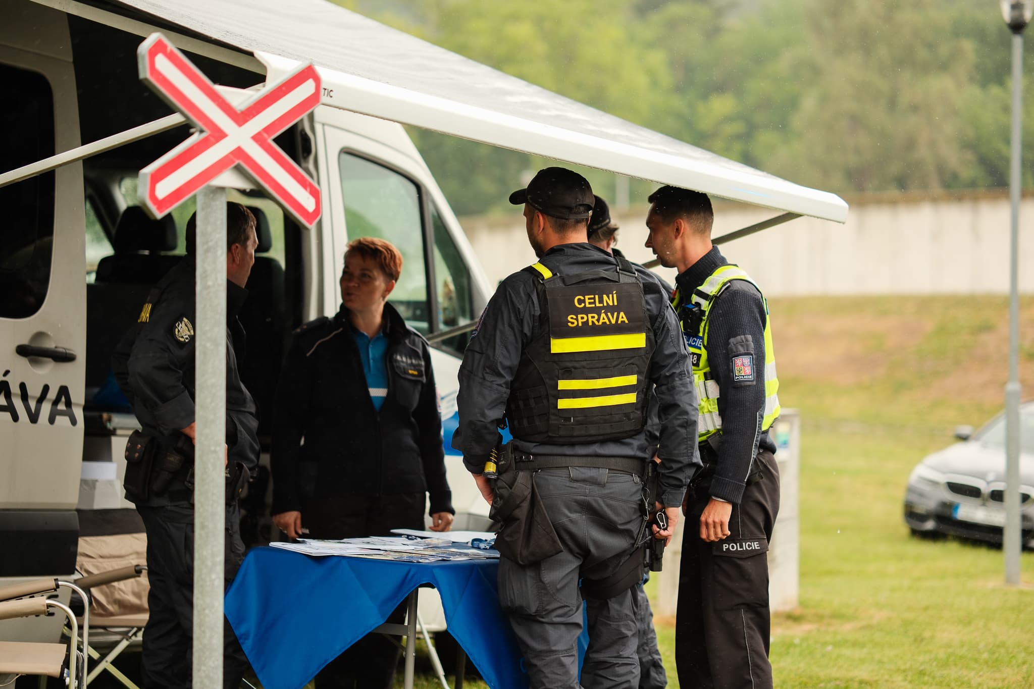 Příslušníci Celní správy a policie diskutují u stánku s dodávkou na louce