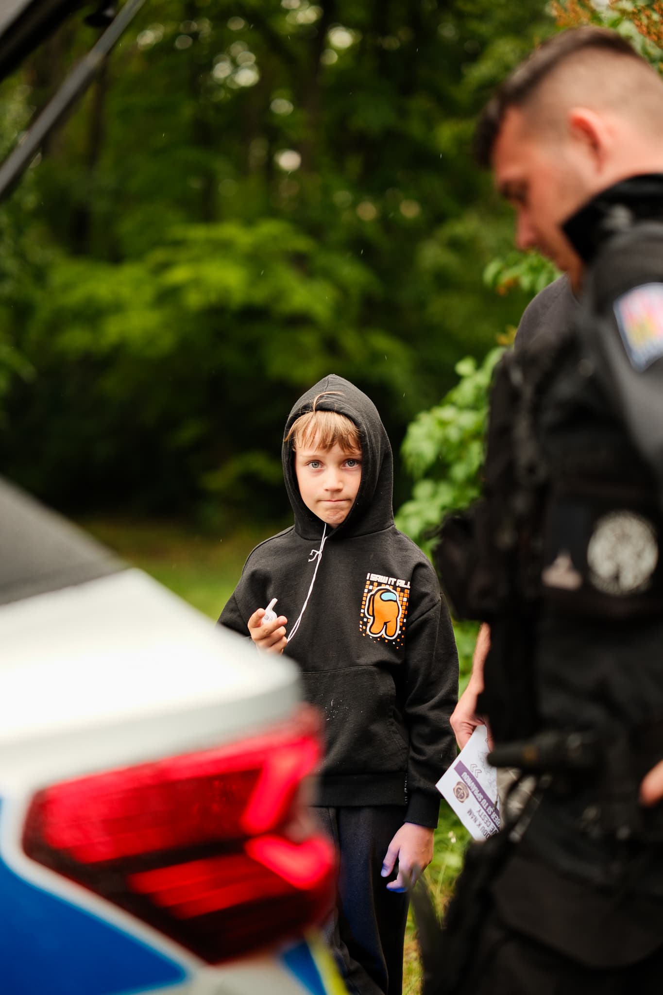 Chlapec v černé mikině s kapucí hovoří s policistou u služebního vozu