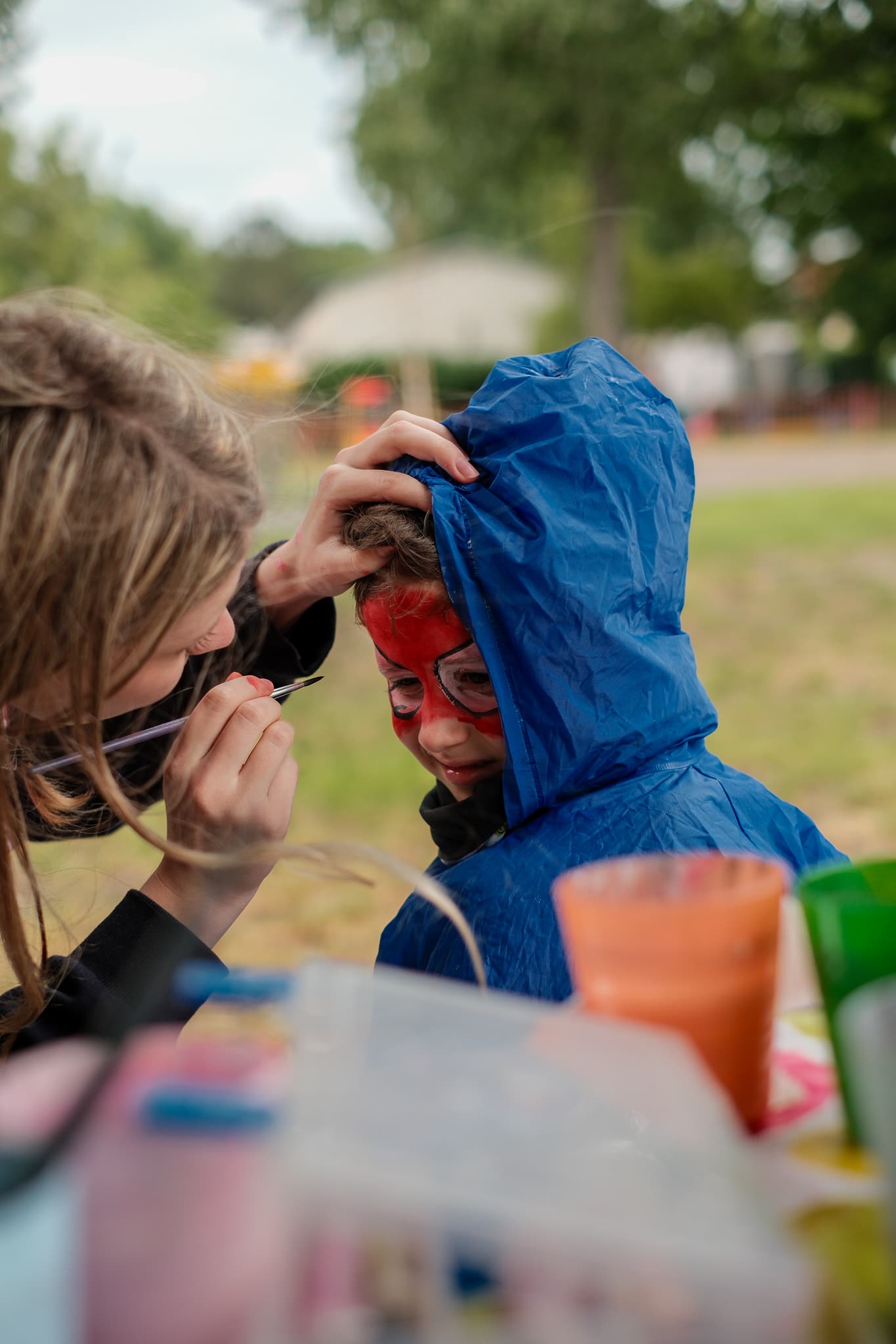 Malování na obličej, dívka vytváří dítěti červenou masku Spidermana u stánku