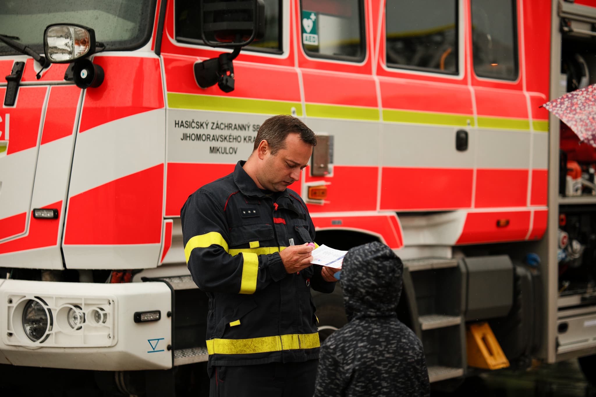 Hasič Jihomoravského kraje rozdává dítěti samolepku před zásahovou cisternou